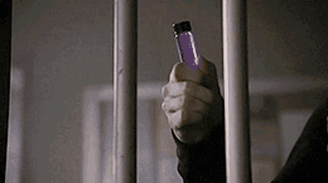 a person is holding a purple lighter behind bars