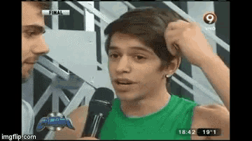 a young man in a green tank top is being interviewed by a man on a television show .