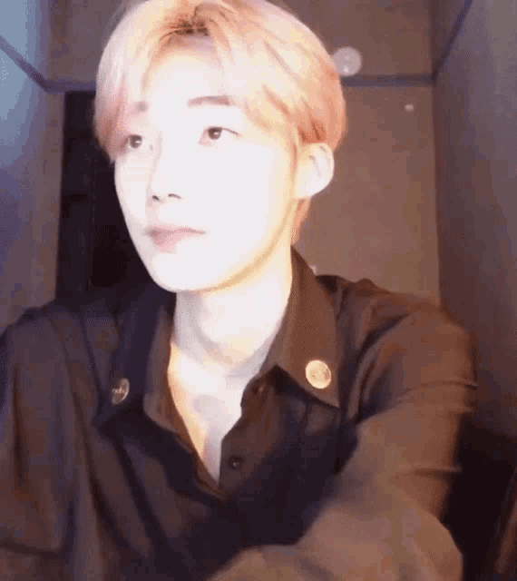 a young man with pink hair and a black shirt is sitting in a dark room .