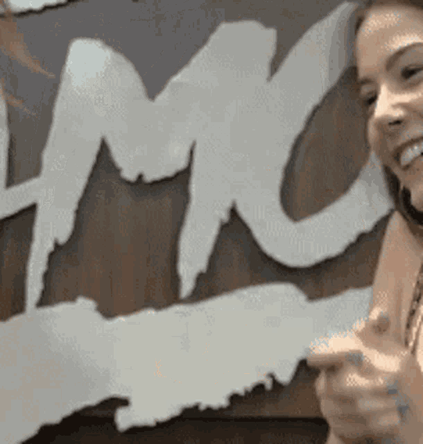 a woman is smiling in front of a sign that says ' lmc ' on it .