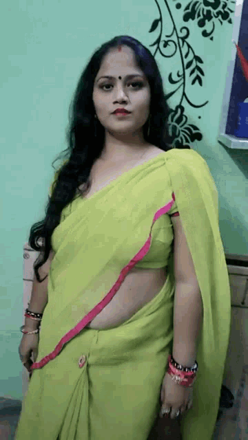 a woman in a green saree is standing in front of a green wall with flowers on it