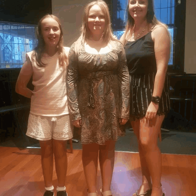 three girls are posing for a picture and one of them is wearing a black tank top