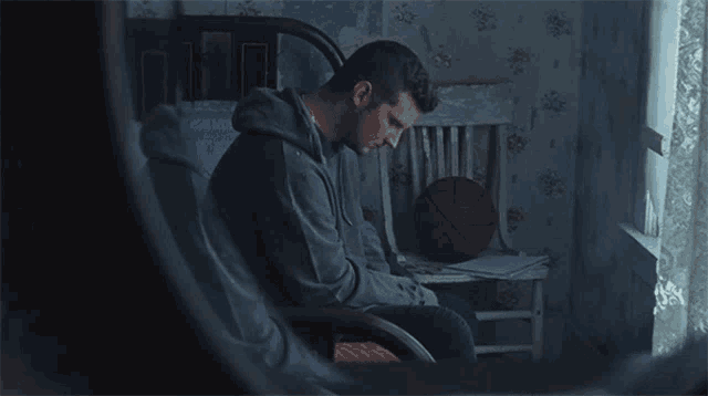 a man sits in a chair looking out a window with a basketball in front of him