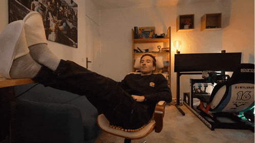 a man sits in a chair with his feet up in front of a sign that says sparco 16