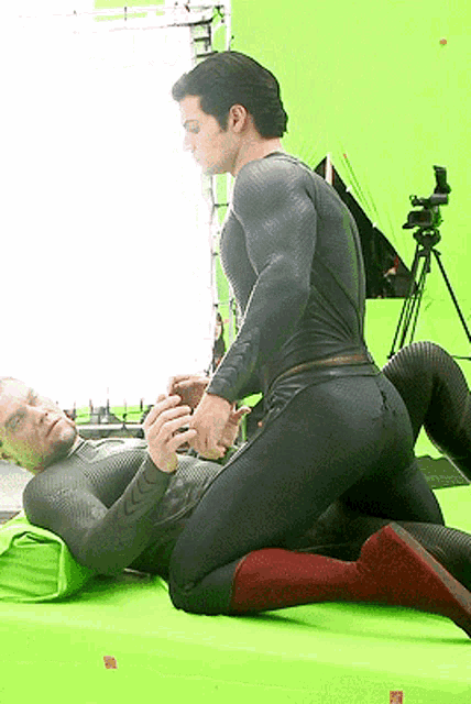 a man in a superhero costume is kneeling on another man 's lap