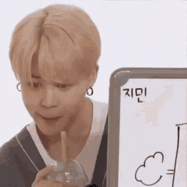 a young man is drinking from a cup with a straw while sitting in front of a white board .