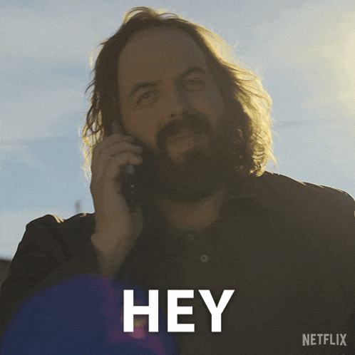 a man with long hair and a beard is talking on a cell phone with the word hey written below him