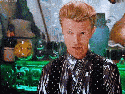 a man in a shiny suit and tie is standing in front of a green table with bottles on it .