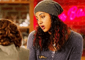 a woman with curly hair wearing a beanie and a shirt that says um