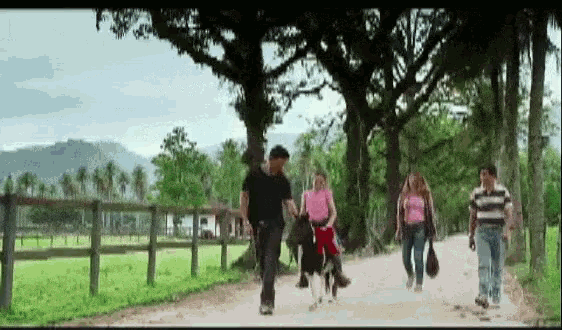 a group of people walking down a dirt road with trees in the background