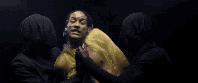 a man with dreadlocks and a yellow cape is surrounded by two men
