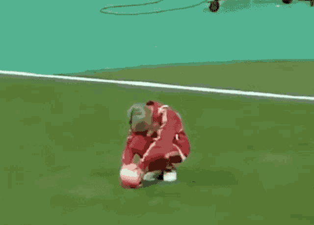 a man in a red jacket is kneeling on a soccer field holding a soccer ball .