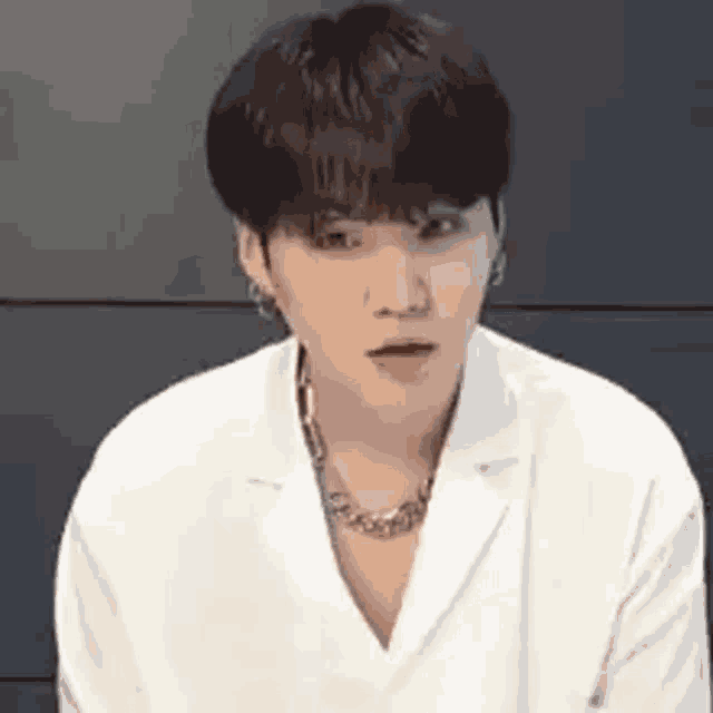 a young man wearing a white jacket and a necklace is sitting down .