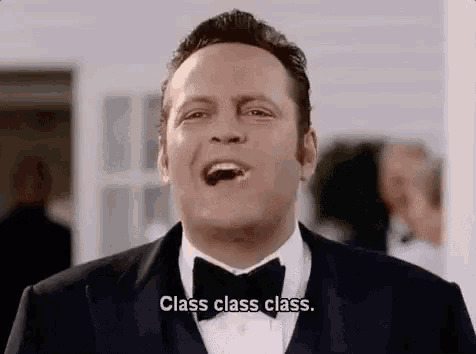 a man in a tuxedo and bow tie is laughing and holding a piece of chocolate in his mouth .