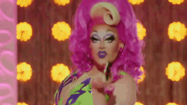 a drag queen with pink hair is holding a green frog in her hand .