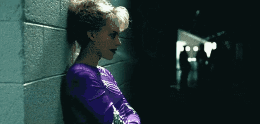 a woman leaning against a wall with a purple shirt on