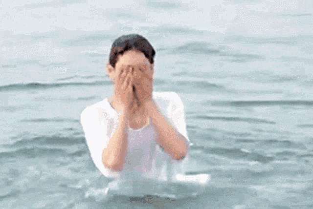 a man in a white shirt is standing in the ocean holding a frisbee .
