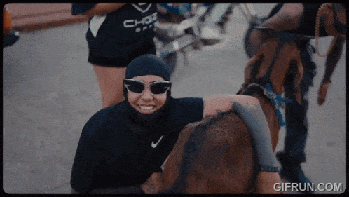 a person wearing sunglasses and a black nike shirt is hugging a horse
