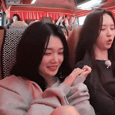 two girls are sitting on a bus with their eyes closed and one is smiling