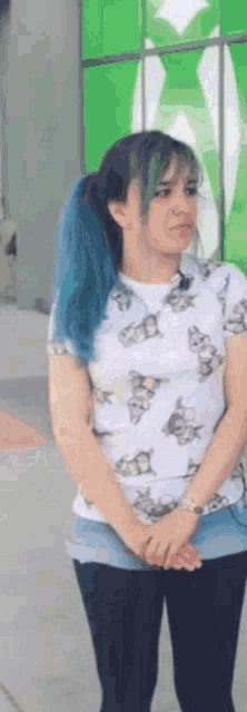 a woman with blue hair and a white shirt is standing in front of a green sign .
