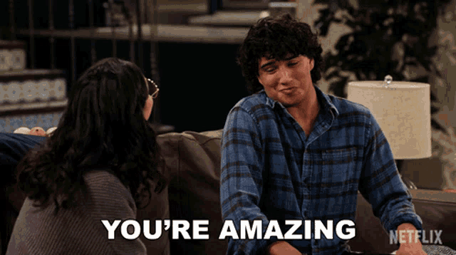 a man sits on a couch with a woman and says you 're amazing on the screen