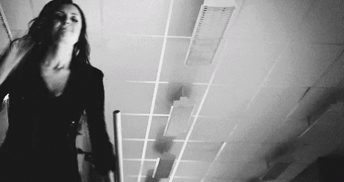 a black and white photo of a woman standing in a hallway with a cane .