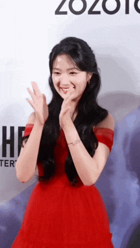 a woman in a red dress is smiling and clapping her hands .