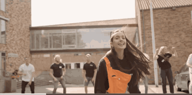 a woman in an orange vest is dancing in front of a group of people