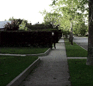 a man in a mask walks down a sidewalk in a neighborhood