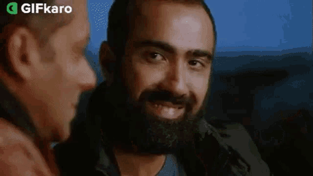 a man with a beard is smiling at another man in a movie .