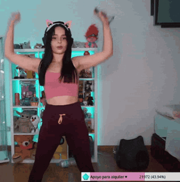 a girl in a pink top and purple pants is dancing in front of a shelf with stuffed animals on it