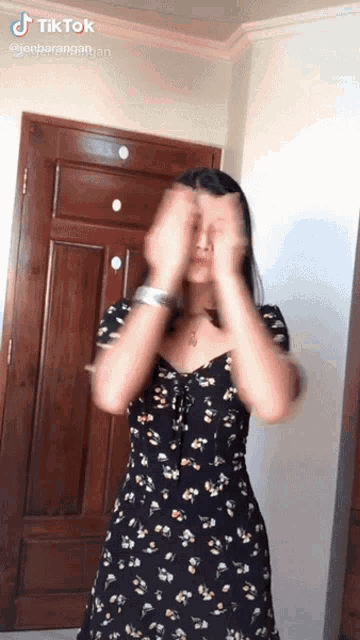 a woman in a black floral dress is dancing in front of a wooden door with tiktok written in the corner