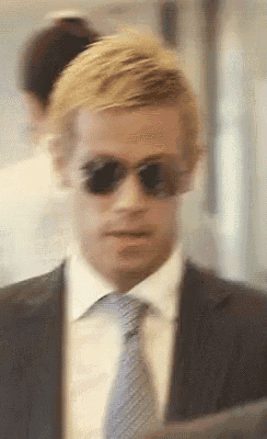 a man in a suit and tie wearing sunglasses looks at the camera