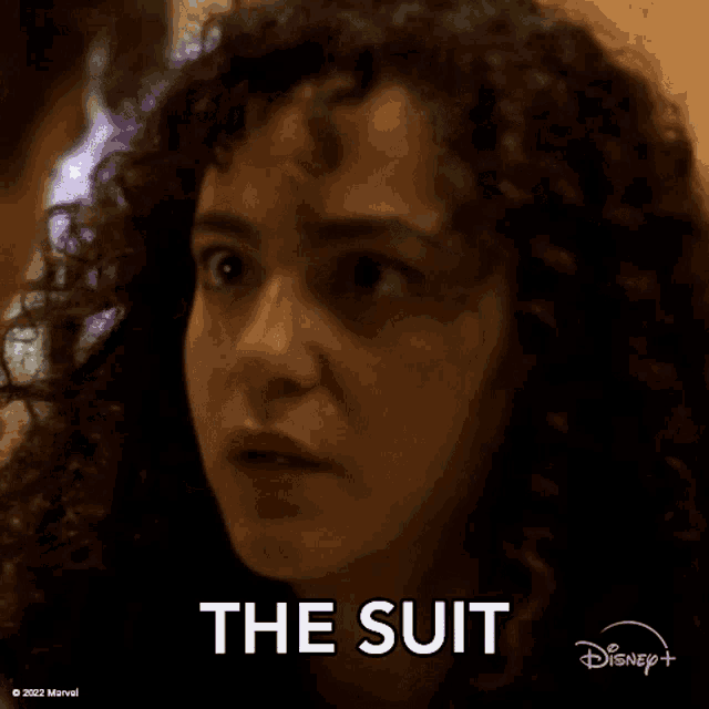 a woman with curly hair is making a funny face and the word the suit is on her face .