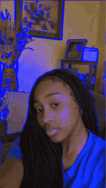 a woman in a blue shirt is taking a selfie in front of a wall with pictures on it .