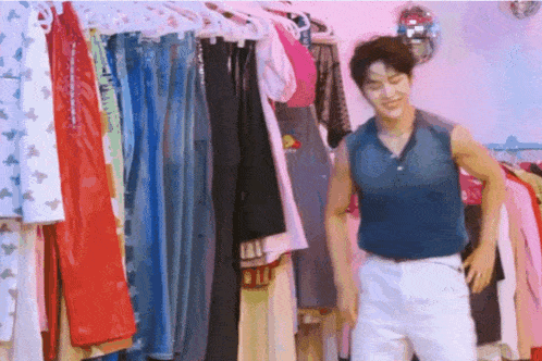 a man in a blue tank top is standing in front of a closet full of clothes