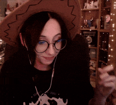 a woman wearing a cowboy hat and glasses has a black shirt with a cow on it