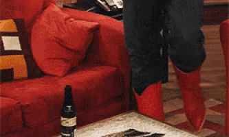 a woman in red boots is sitting on a red couch next to a table with a bottle of beer on it