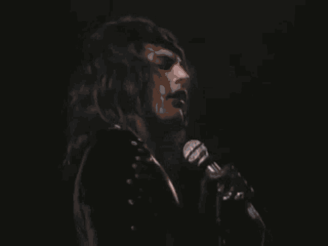 a man is singing into a microphone on stage in a dark room .