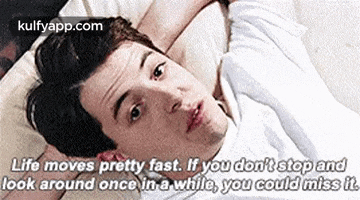 a man is laying on a bed with a quote about life moving fast .
