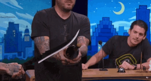 a man is holding a knife in front of a microphone while another man sits behind him .