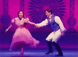 a man and a woman are dancing on a stage in front of a purple background .