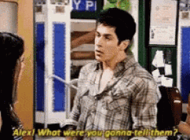 a man in a plaid shirt is talking to a woman in a room and says alex what were you gonna tell them ?