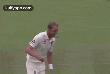 a man in a white shirt is laughing with his mouth open on a cricket field .