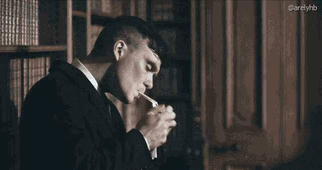 a man in a suit is smoking a cigarette in front of a bookshelf .