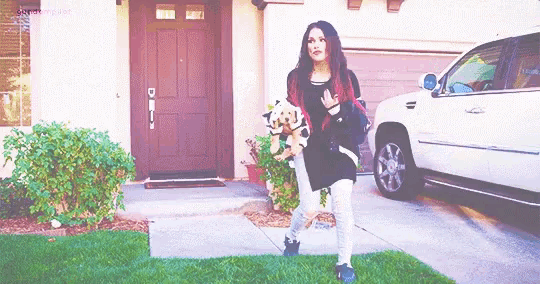 a woman carrying two dogs is standing in front of a house