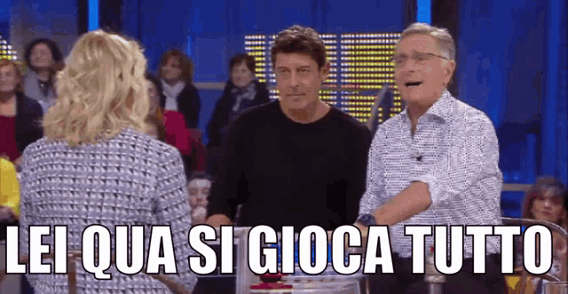 two men and a woman are standing in front of a crowd with lei qua si gioca tutto written above them
