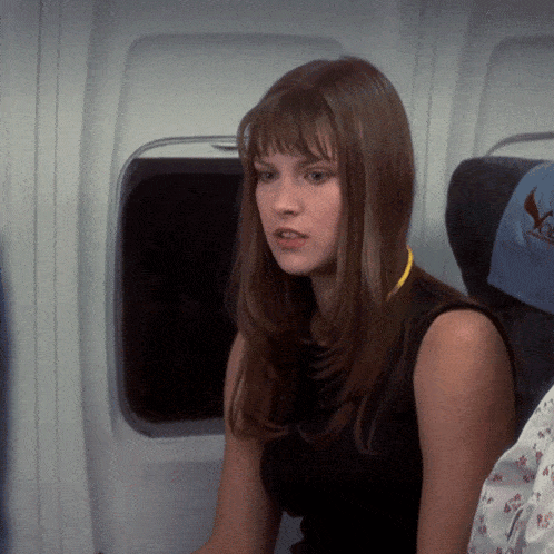 a woman in a black tank top sits in a plane seat with a blue blanket on it