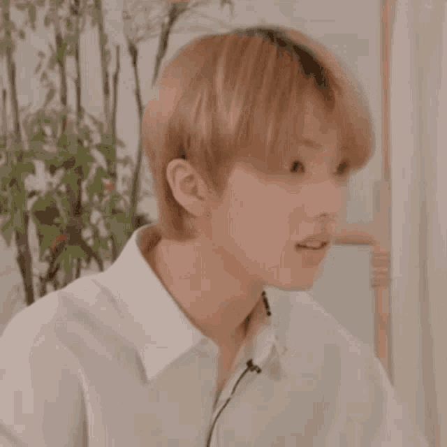 a young man with blonde hair is wearing a white shirt and a microphone in his ear .
