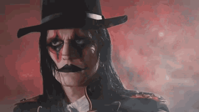 a man with long hair and a hat is wearing a clown costume and looking at the camera .